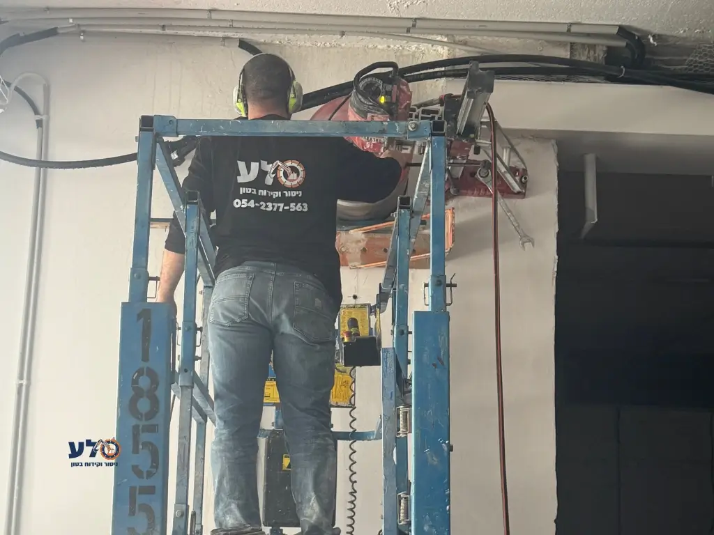 עובד של סלע מבצע קידוח בטון בקיר באמצעות ציוד הרמה